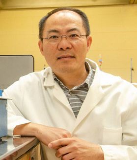 Headshot of WVU researcher Lance Lin. He is standing in a lab space wearing a white lab coat over a gray and white striped shirt. He has short black hair and wears glasses. 