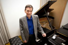Man in a gray suit and blue shirt posing next to a piano