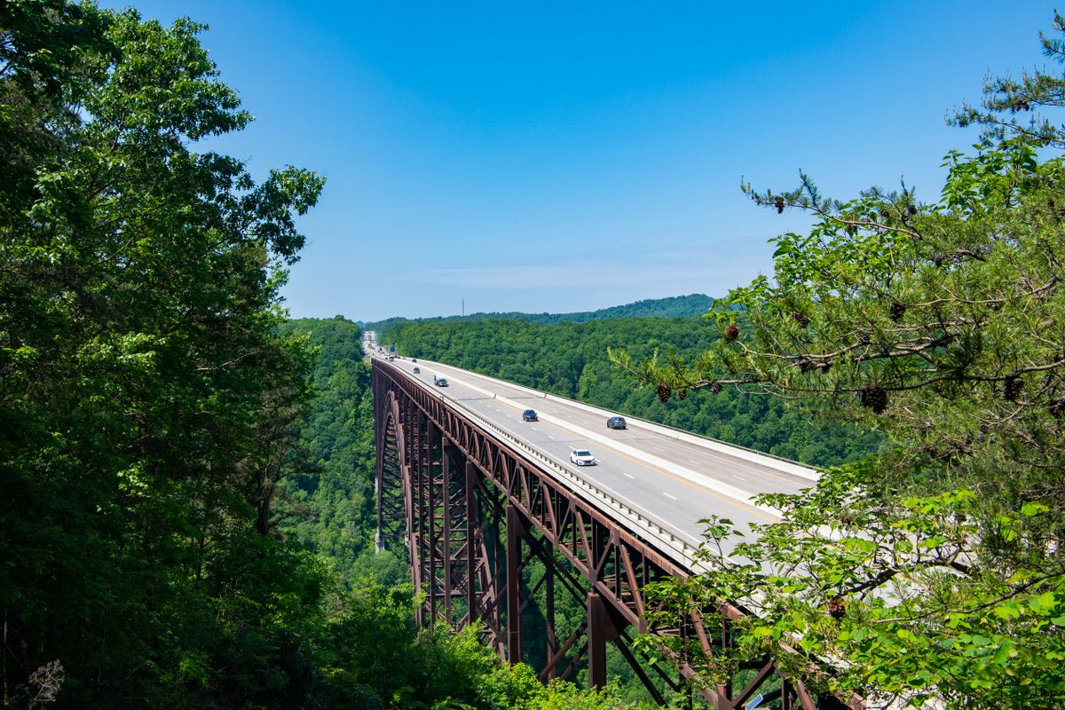 The New River Gordge Bridge has cars traveling over it surrounded by green trees