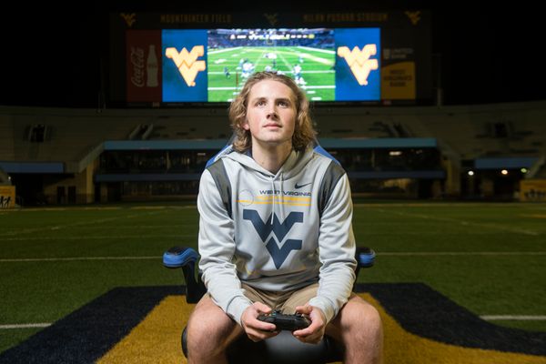 young man in flying WV shirt with hood, large screen in background