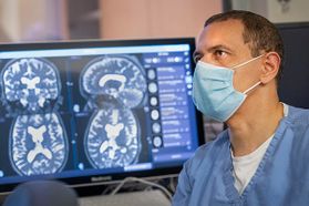 man in medical mask with computer screen of brain images in the background