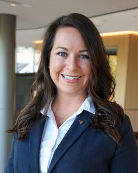 Headshot of WVU employee Tara St. Clair. She is pictured inside wearing a navy blue jacket over a white collared dress shirt. She has long brown hair. 