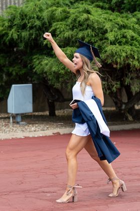 woman in white dress puts her fist in the air to celebrate graduation
