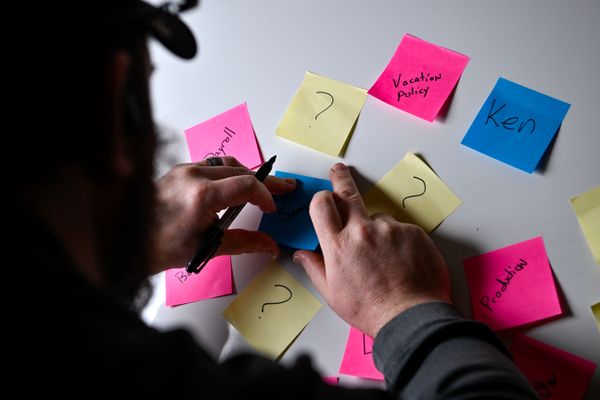 Colorful post it notes are scattered around a table as the silhouette of a person looks at them and marks notes on them. 