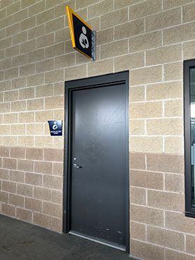 A photograph showing a newly opened lactation room inside Milan Puskar Stadium on the WVU campus. The dark brown door is closed and has a graphic sign above it and on the wall next to it. 