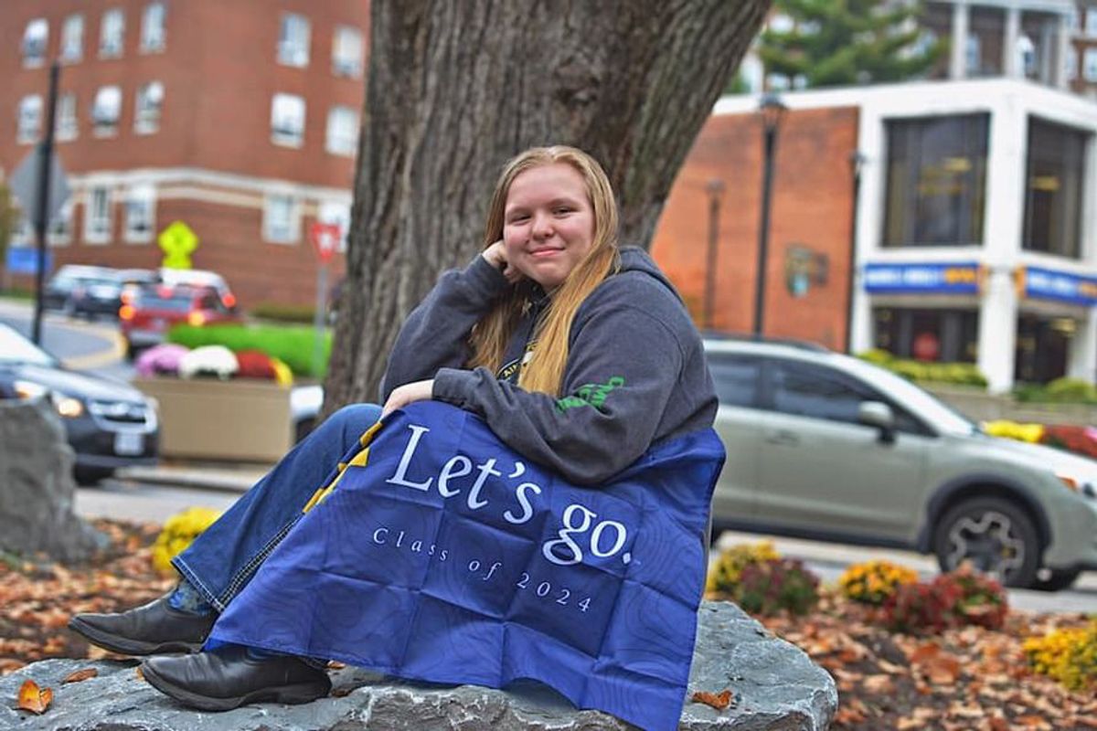 young woman smiling with WVU flag on her lap