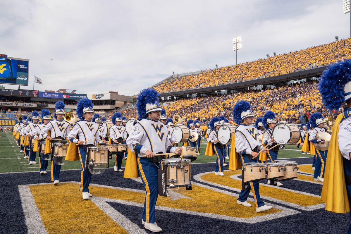 Image featuring the WVU marching bang performing on the field during a football game. The drum line is in the photo. 