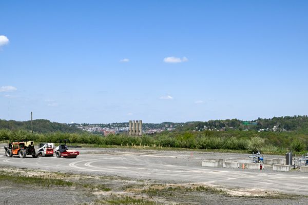 A geothermal well pad site in Morgantown, West Virginia. The area has been cleared for drilling and pieces of heavy equipment remain on site. There are green hills in the background and blue sky. 