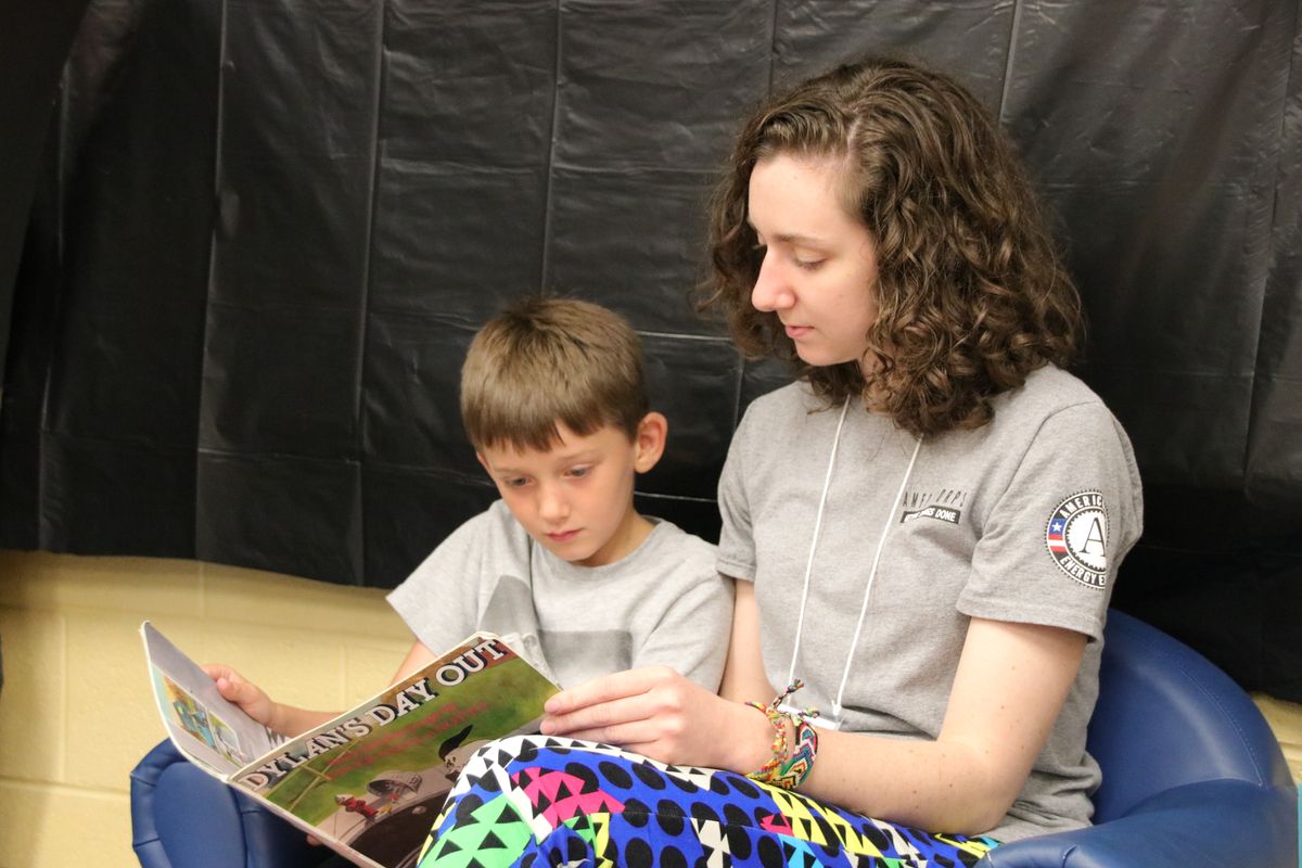 A young woman in a gray t-shirt reads to a boy