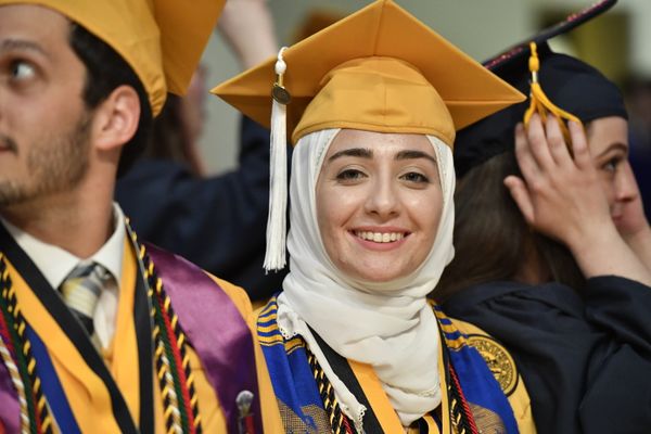 young woman in white hijab and gold mortarboard smiles at the camera