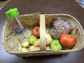 A wicker woven basket with a clear and green water bottle and seeds and tomatoes. 
