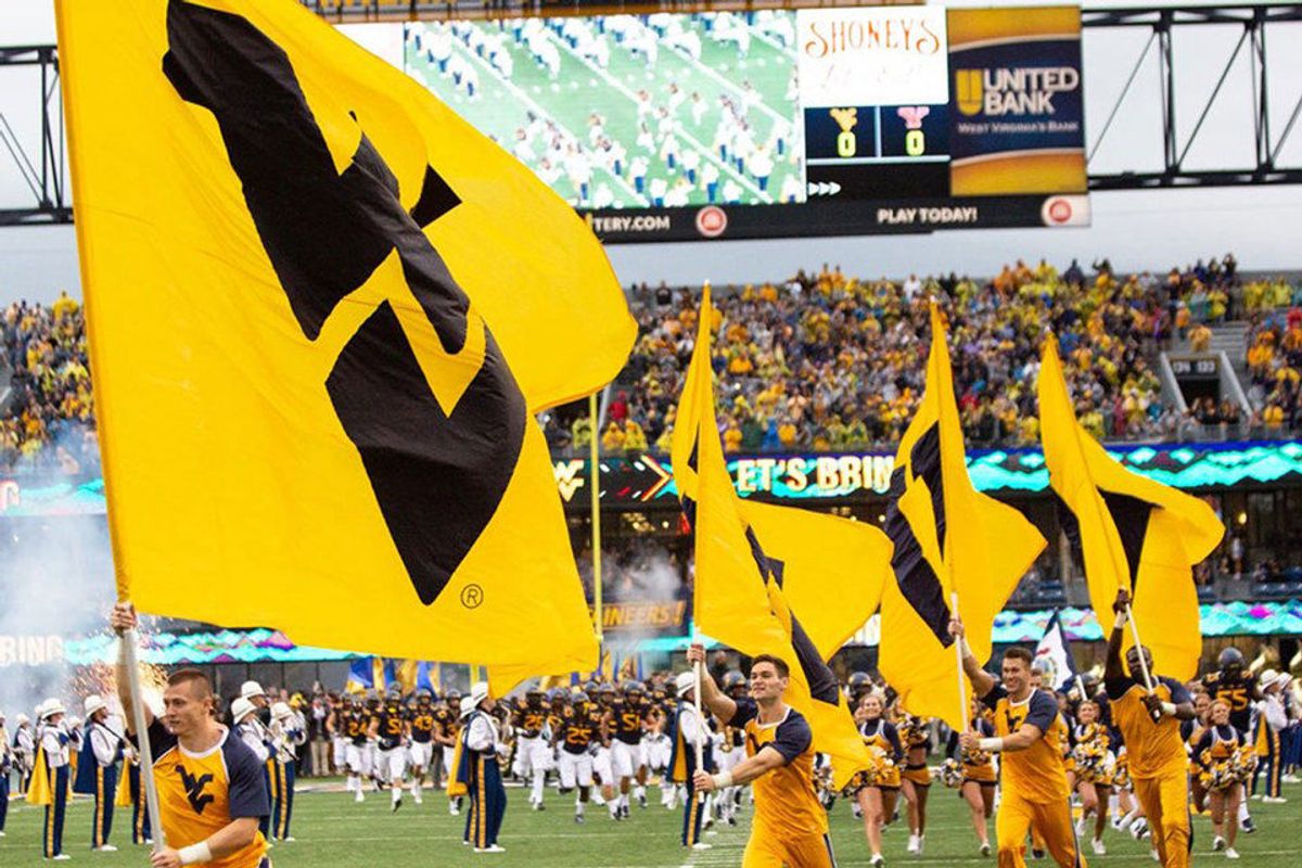 WVU cheerleaders carry WVU flags on Mountaineer Field during a football game.