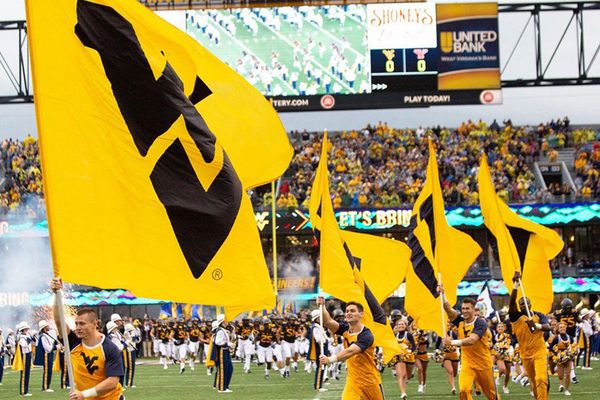 WVU cheerleaders carry WVU flags on Mountaineer Field during a football game.