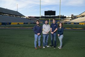 This is a wide shot showing the four finalists to be the 69th Mountaineer mascot standing with their arms crossed. In the background is Milan Puskar Stadium on a warm, sunny day.