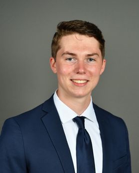 Headshot of WVU student Austin Braniff. He is pictured against a gray background wearing a navy blue suit, white dress shirt and navy blue tie. He has short, brown hair/ 