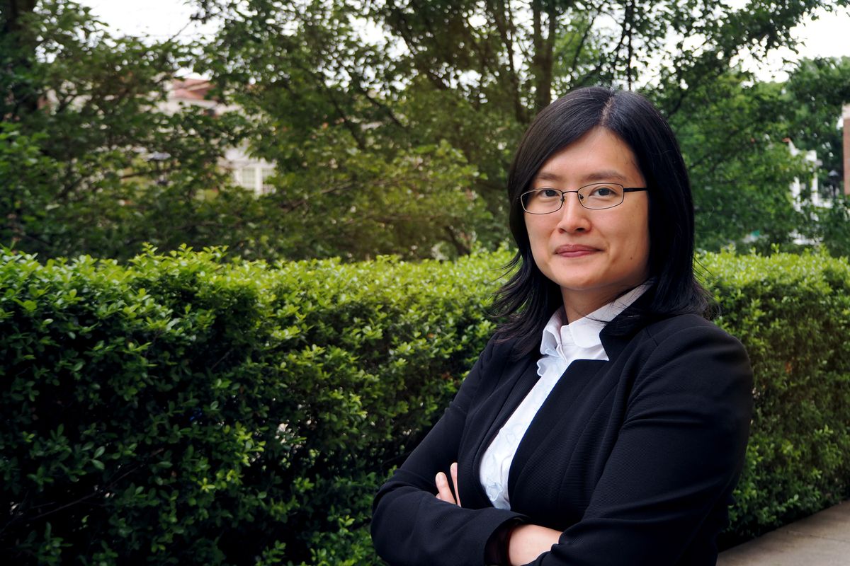Woman with black hair wearing a black blazer and glasses with her arms crossed.