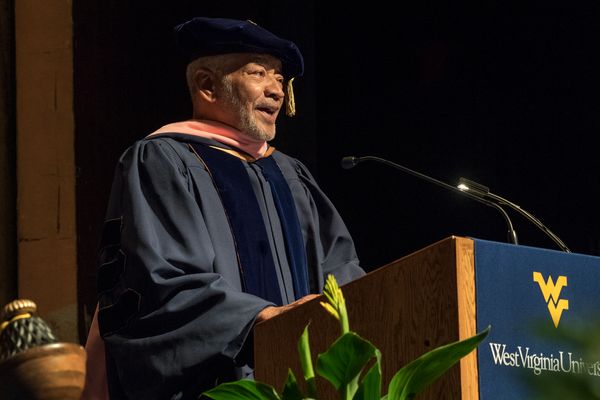 man in commencement garments speaks at podium 
