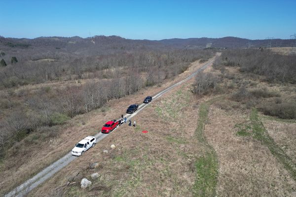 A drone image showing four vehicles parked on a road in a remote area. 