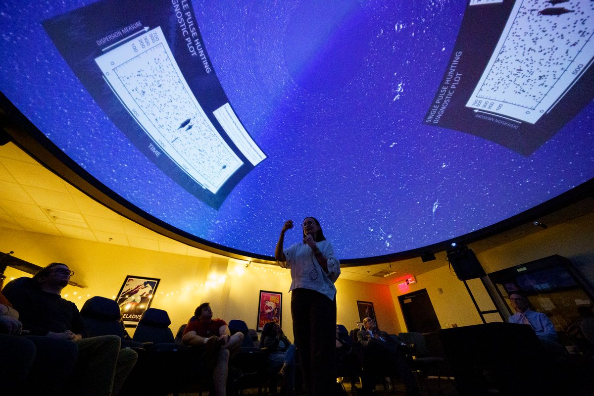 WVU astrophysicist Maura McLaughlin is show giving a presentation in the WVU Planetarium. The ceiling is illuminated above her and the seats are full of spectators. 