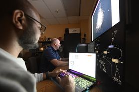 A student and his professor sit together in a dark lab looking at screens for the research they are conducting. 