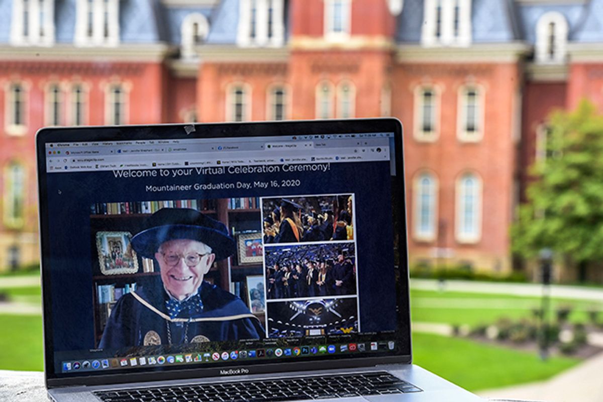 laptop computer screen with man in graduation regalia in front of large brick building