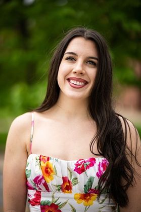 Headshot of WVU Fulbright Scholar Abigail Dorsa. She is pictured outside wearing a floral printed spaghetti strap dress. She has long dark colored hair. 