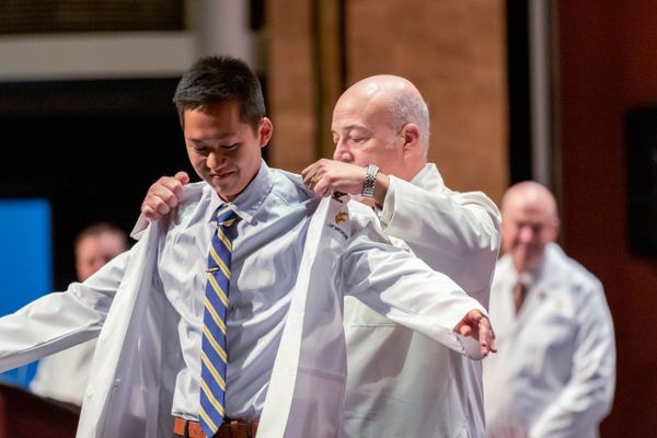 A WVU medical student receives his white lab coat from a WVU School of Medicine faculty member. 