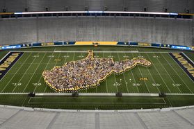Students stands in the middle of the marching band shaped like the state of West Virginia