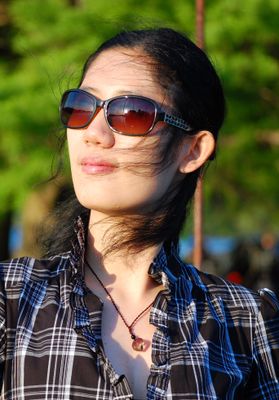 Portrait shot of Xinyu Zhang. She is pictured outdoors wearing sunglasses and wind slightly blows her hair.