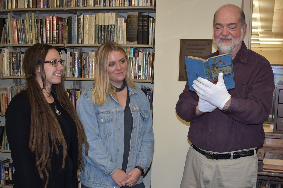 Harold Forbes, retired rare books curator, peruses a book dealer Jim Presgraves donated to WVU Libraries in honor of Forbes as library associate Autumn Summers and work study student Jamie Rood look on.