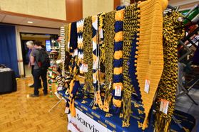 An arts and crafts show on the WVU campus during Mountaineer Week. A booth full of WVU-themed knitted scarves is shown in the photo. 