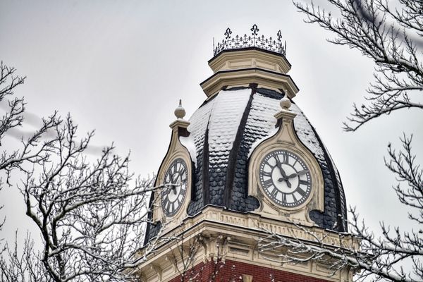 clock tower, snow dusted, branches in foreground. 