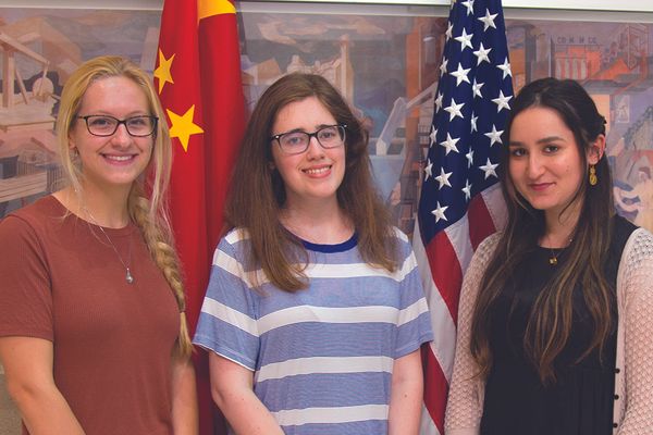 Three young women stand in front of China/American flags