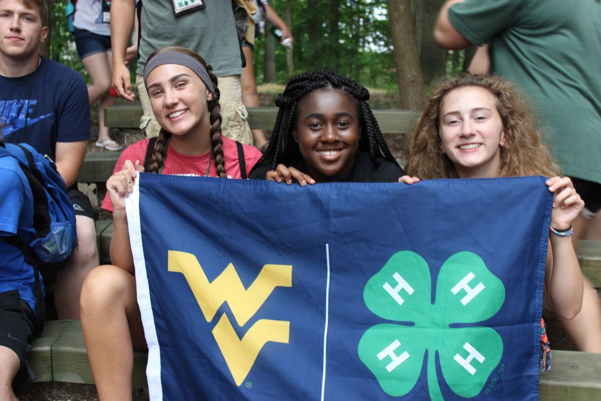 three young woman hold a blue, gold and green flag