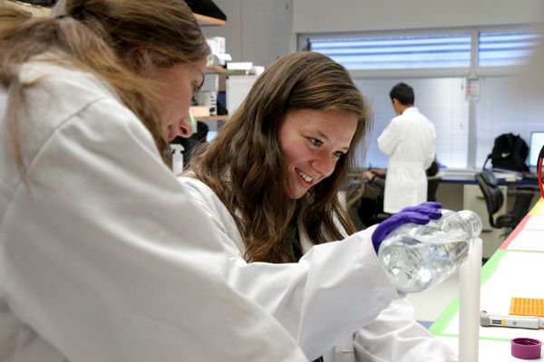 young woman in lab, woman looking over her shoulder, man in background