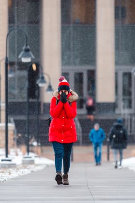 WVU student in red coat covers face with gloved hands to stay warm.