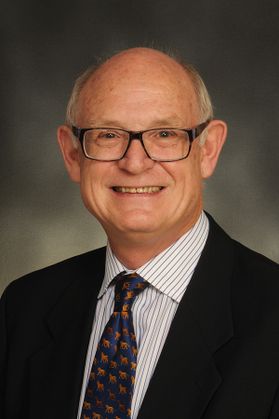 Portrait shot of a smiling Gordon Smith, he is pictured wearing a suit with a patterned tie and glasses.