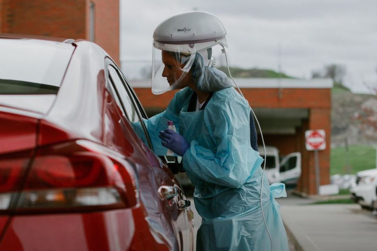 Healthcare worker in suit testing a potential COVID-19 patient in a red car