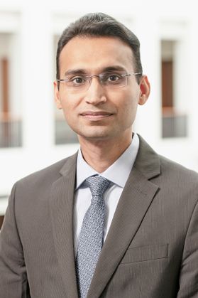 Headshot of WVU professor Pawan Jain. He is pictured inside of a building with white columns behind him. He is wearing a taupe colored suit with a white dress shirt and gray tie. He has short brown hair and wears glasses. 