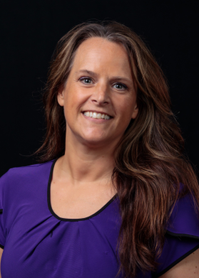 A person is shown from the shoulders up. The person has long brown hair and is wearing a purple short sleeve top in front of a black backdrop.