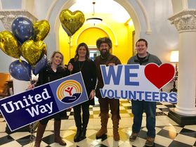 Four people celebrate United Way with balloons, signs and the WVU Mountaineer
