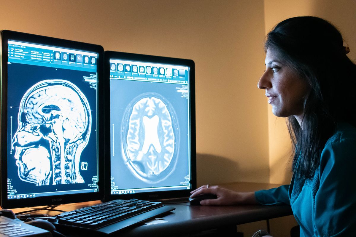 woman looks at computer screens with showing images of a human brain