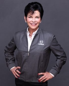 Headshot of owner and CEO of 84 Lumber and Nemacolin Maggie Hardy. She is standing against a gray background wearing a gray, zip-up 84 Lumber jacket over a white dress shirt. She has short, dark hair.  