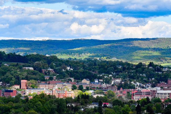 The WVU Downtown and Evansdale Campuses are shown at a distance with hills in the background under blue skies.