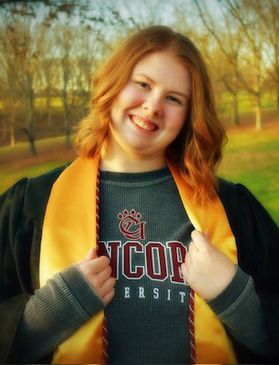 Photograph of scholarship recipient Madison Taylor. She is pictured outside wearing a university-branded sweatshirt under her commencement sashes and chords. She has shoulder length auburn hair. 