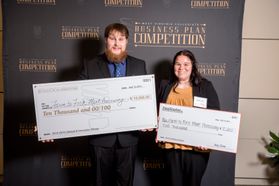 Two people hold large checks