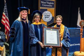 three women stand with a framed college degree on a stage