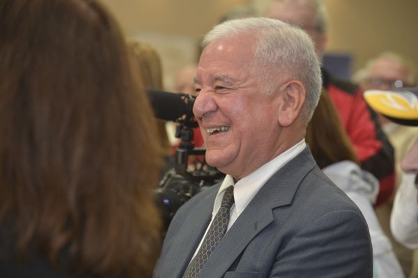 Former Congressman Nick Rahall stands in with a group of people. He has a big smile on his face and is wearing a gray suit with a white dress shirt. He has white hair.