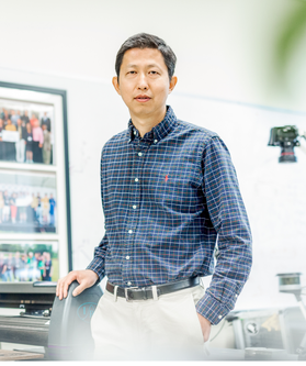 Yu Gu, and associate professor in the Department of Mechanical and Aerospace Engineering is pictured standing in his lab wearing a blue shirt and khakis. 
