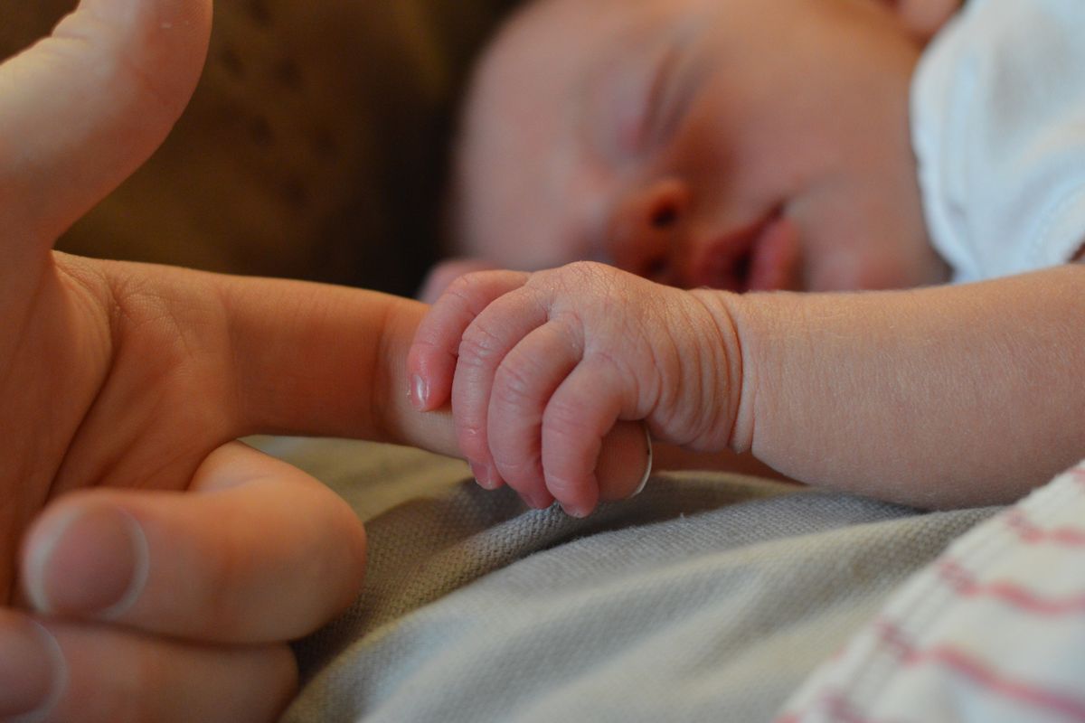 An infant's hand holds an adult's finger.